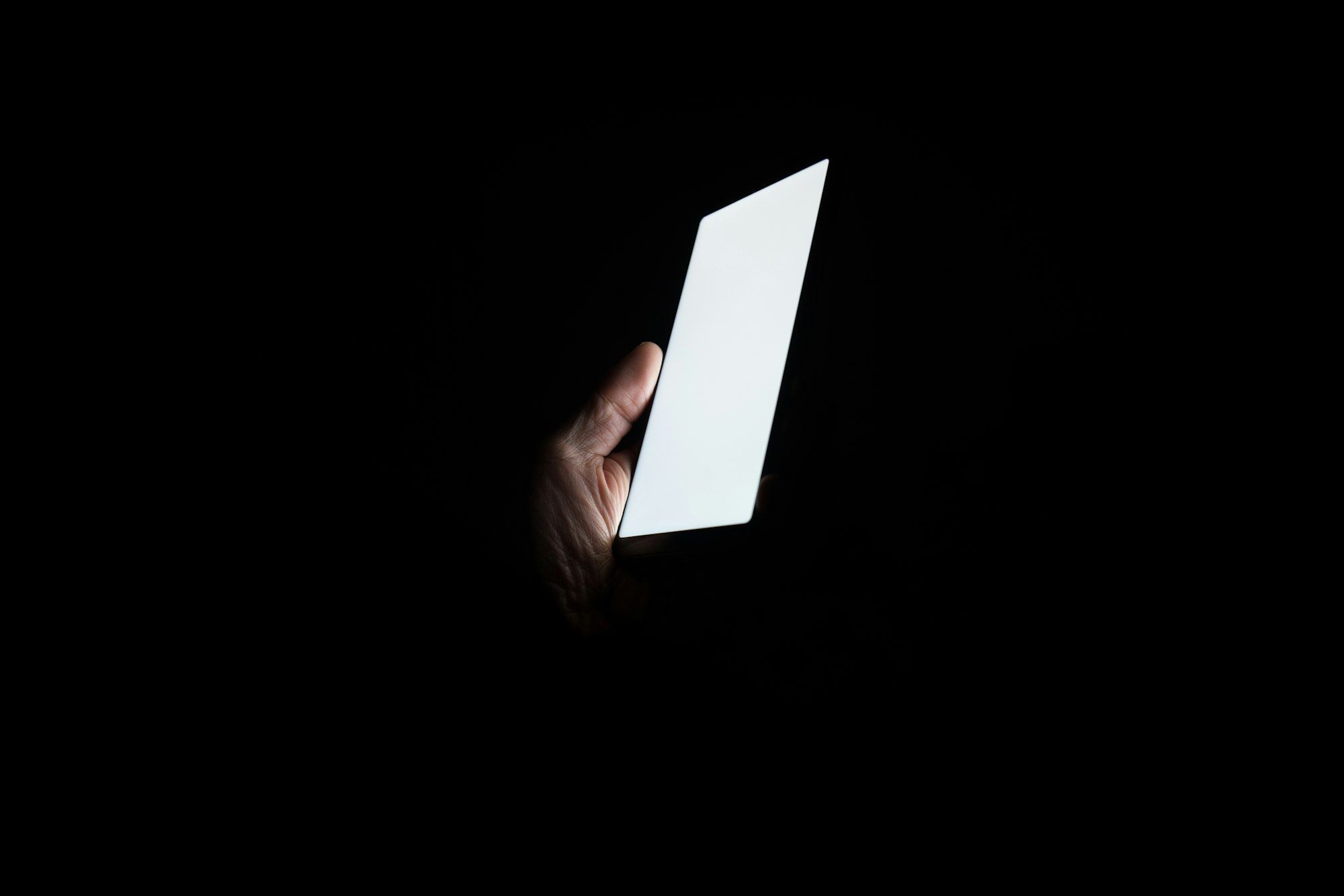A hand holding a glowing phone in the dark